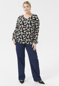Blusa negra con estampado floral, de manga larga y escote en V, combinada con vaqueros de pierna ancha azul oscuro y zapatos de punta negra.