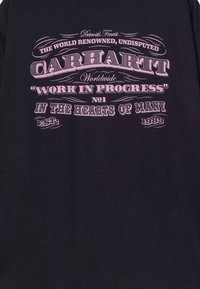 Czarny bawełniany t-shirt z różowym nadrukiem. Tekst zawiera "Carhartt", "Work in Progress" oraz "est. 1989", z dekoracyjnymi elementami.