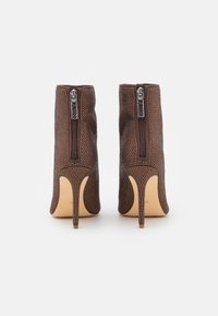 Brune ankelstøvler med en tekstureret overdel, der har lynlås bagpå og en stilet hæl. Detaljeret med små perforeringer.