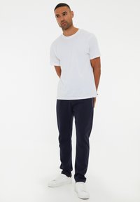Camiseta blanca de algodón combinada con pantalones de chándal azul marino y zapatillas blancas. Cuello redondo simple, corte relajado y textura de tela suave.