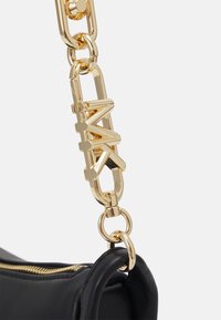 Zbliżenie czarnej skórzanej torby z złotym suwakiem i masywnym złotym paskiem łańcuchowym z zapięciem w kształcie logo MK.