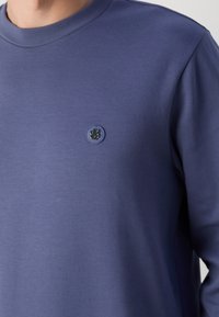 Marinblå sweatshirt med rund hals och långa ärmar. Den har en liten logopatch på bröstet, tillverkad av mjukt och slätt tyg.