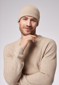 Beanie e maglione a coste color beige. Il tessuto lavorato presenta una scollatura rotonda e maniche lunghe, evidenziando un aspetto morbido e caldo.