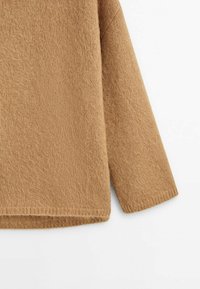 Gros plan d'un pull en maille à manches longues de couleur camel avec une texture douce et duveteuse, des poignets et un ourlet côtelés, sur un fond blanc.