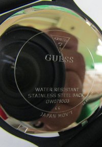 Stražnja strana Guess sata od nehrđajućeg čelika. Ugravirani tekst uključuje "OTPORNOST NA VODU", broj modela i "JAPANSKI MEHANIZAM". Okrugli oblik s crnom narukvicom.