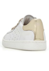 Sneaker bianco con dettagli perforati, accenti dorati sul tallone e lacci beige. Punta arrotondata, suola piatta in gomma e texture liscia.