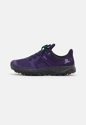 Lilla og sort lavskåret Salomon trail løbesko med grønne snørebånd, plettet sort sål og synlige Gore-Tex- og Contagrip-mærker.