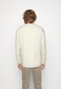 Camicia a maniche lunghe di colore giallo chiaro in tessuto di cotone, con colletto button-down e polsini con bottone, indossata con pantaloni in corduroy beige.