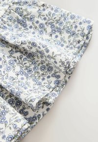 Tela blanca con pequeño estampado floral azul y verde, con pliegues y bordes cosidos sobre un fondo claro.