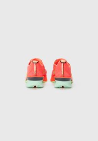 Bright red running shoes feature a textured upper, reflective accents, and a green outsole. Heel tab is black with logo detail.