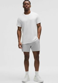Vit kortärmad sporttröja med ett texturerat mönster, i kombination med ljusgrå shorts och vita sportskor. Enkelt design, modern passform.