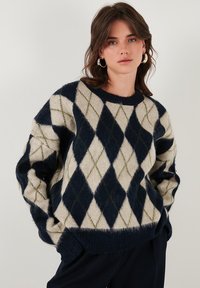 Maglione a maglia con un motivo argyle blu navy, crema e oliva. Tessuto morbido e testurizzato con collo rotondo e vestibilità rilassata.