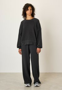Ensemble en sweat-shirt noir et pantalon large en tissu doux. Présente une coupe décontractée, un col côtelé et des coutures minimales.