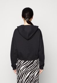 Sudadera corta negra con una gran capucha suave y dobladillo acanalado. Llevada sobre una falda a rayas de cebra en blanco y negro. Material de algodón suave.
