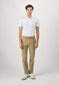 Camisa polo blanca, pantalones chinos beige y zapatillas blancas con detalles en marrón. El conjunto es casual, con un corte clásico y un diseño sencillo.