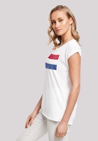 White short-sleeve T-shirt featuring red and blue horizontal stripes across the chest, made of soft cotton material with a relaxed fit.