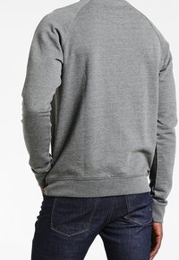 Felpa grigia con collo rotondo in misto cotone, con maniche raglan e polsini a coste, abbinata a jeans in denim scuro.