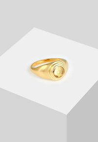 Goldring mit einem auffälligen runden gelben Stein, umgeben von konzentrischen Bändern. Glatte, polierte Oberfläche und abgerundete Kanten.