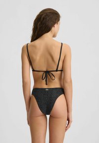 Bikini nero con spalline sottili, chiusura con legatura sulla schiena e slip a vita alta con una sottile texture e un accento in oro sul retro.