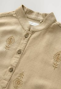 Beige Baumwollhemd mit Stehkragen, ausgestattet mit drei braunen Knöpfen und floralen Stickereien auf der Vorderseite. Weicher, strukturierter Stoff.