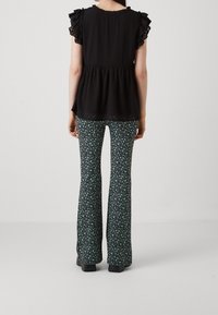 Haut noir texturé avec des manches volantes, associé à un pantalon évasé présentant un motif floral vert sur fond sombre.