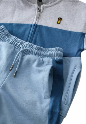Blauer und grauer Reißverschluss-Pullover mit einem Hummer-Patch, kombiniert mit passenden blauen Jogginghosen mit elastischem Bund und Taschen.