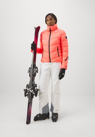 Helles orange Puffermantel mit gestepptem Design, kombiniert mit weißen Skihosen mit grauen Akzenten. Schwarze Handschuhe und Skiausrüstung sind enthalten.