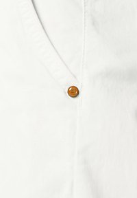 Weißes Shirt mit V-Ausschnitt, das mit einem einzelnen orangen Knopf und subtiler Struktur versehen ist. Der Stoff ist glatt und leicht.