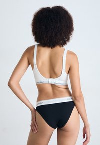 Bijeli grudnjak s podesivim naramenicama i Calvin Klein logotip trakom, u kombinaciji s crnim gaćicama visokog struka s bijelom logotip trakom.