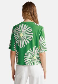 Top corto verde con grandes patrones florales rosas y centros verde claro. Mangas cortas, material de algodón, ajuste casual y escote amplio.