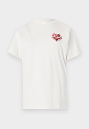 T-shirt en coton blanc à col rond, avec un graphique en forme de cœur rouge portant le mot "HUGO" à l'intérieur. Manches courtes, coupe décontractée.