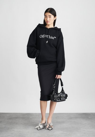 Černá oversized mikina s bílým logem "Off-White", kombinovaná s úzkou černou midi sukní, metalickými botami s mašlí a černou kabelkou se studny.