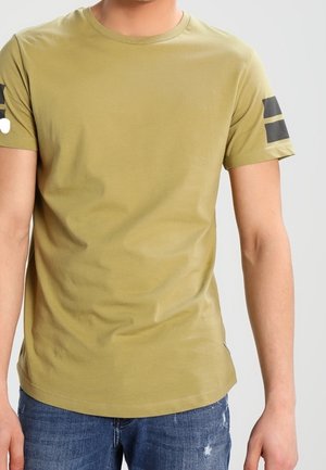 Olijfgroene katoenen t-shirt met een ronde hals, korte mouwen en zwarte gestreepte accenten op de schouders. Gladde textuur, slim fit. Spijkerbroek zichtbaar.