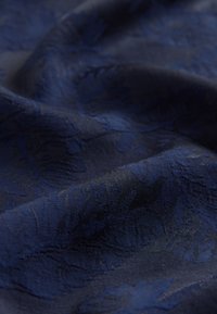 Tissu bleu marine présentant un motif floral texturé, avec une finition lisse et un éclat subtil, affichant des plis drapés et de la profondeur.