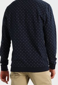 Felpa blu navy con un piccolo motivo geometrico ripetuto, polsini e orlo a coste, e una finitura morbida e testurizzata.