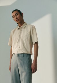 Korte mouwen beige blouse met kraag en een borstzak, gecombineerd met lichtgrijze op maat gemaakte broek met een gladde textuur en plooien.