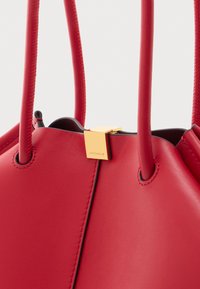 Borsa a mano rossa in pelle con sottili cinturini e una piccola chiusura dorata incisa con il nome del marchio Coccinelle.