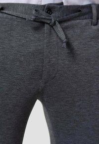 Dark gray joggers made of soft, textured fabric with a drawstring waist and a button closure at the top. Features subtle stitching details.