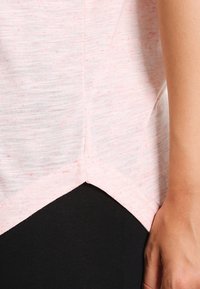 Kurzes, rosa Mélange-Oberteil mit geschwungener Saumlinie und leicht strukturierter Oberfläche. Kombiniert mit schwarzen, figurbetonten Hosen, die eine seitliche Nähte-Detailierung zeigen.