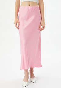 Gonna midi in satin rosa con un design fluido e una vita elasticizzata. Abbinata a scarpe ballerina bianche a punta con un dettaglio a fiocco.