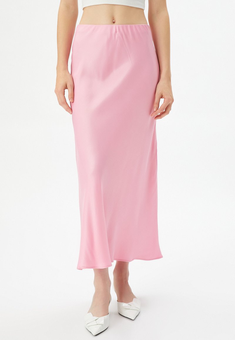 Satin-pinke Midirock mit einem fließenden Design und elastischem Bund. Kombiniert mit weißen spitzen Ballerinas mit einer Schleifendekoration.