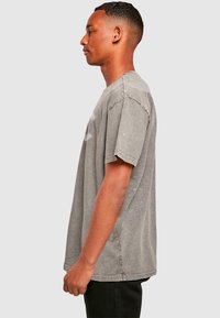 Grå, oversized bomulds T-shirt med korte ærmer, featuring en rund hals og subtilt falmet tekstur. Ingen synlige mønstre eller distinkte accenter.