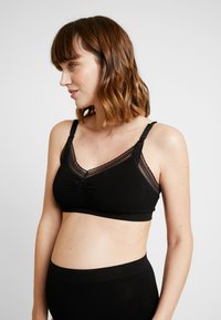 Black bra with a soft fabric, sheer mesh detailing, v-neck design, adjustable straps, and a central knot accent under the bust.