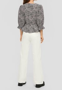 Blusa floreale in bianco e nero con maniche a sbuffo, orlo con volant e design a peplo. Abbinata a pantaloni a zampa bianchi e scarpe con piattaforma nere.