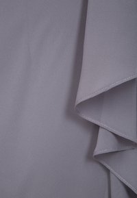 Tissu lavande clair avec une texture lisse, présentant un détail de volants superposés le long d'un bord et des coutures soignées le long de l'ourlet.