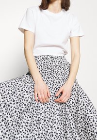 T-shirt blanc à manches courtes associé à une longue jupe fluide ornée d'un motif floral noir sur fond blanc. La jupe a une taille nouée.