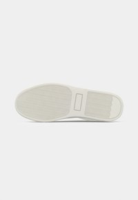 White sneaker sole with textured grip patterns, flat heel, and rectangular detail in the midfoot area against a plain background.