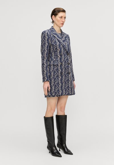 Rochie-blazer cu model marine, cu mâneci lungi și guler șal, având un design geometric în crem. Asortată cu cizme din piele neagră până la genunchi.