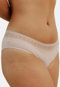 Culotte en coton rose clair avec une taille en dentelle à bord festonné et une texture lisse. Présente une coupe mi-haute et sans coutures visibles.