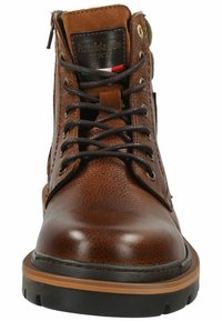 Las botas de tobillo de cuero marrón presentan un upper texturizado, punta redonda, suela de goma negra y un cierre frontal con cordones, ojales de metal y una cremallera.